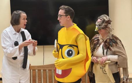 An actor in a :) costume faces two more actors, dressed in a Glasses-emoji costume and as a bird