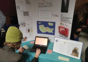 Someone with their back to the camera on a laptop, at a table with a display titled 'The Mino-tour'