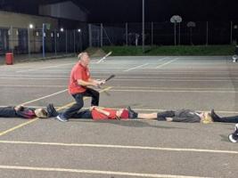 A man juggling clubs while walking up a line of people lying head-to-toe on the ground