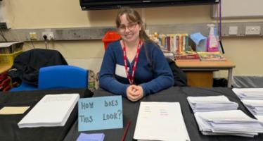 Annick sitting behind a table and smiling. The table's sign says "How Does This Look?"
