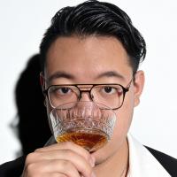 A picture of Maxwell Lu sipping a glass of liqueur, front and centred.