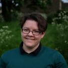 Picture of Emily wearing a black shirt and green jumper. The background is grass.