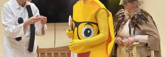 An actor in a :) costume faces two more actors, dressed in a Glasses-emoji costume and as a bird